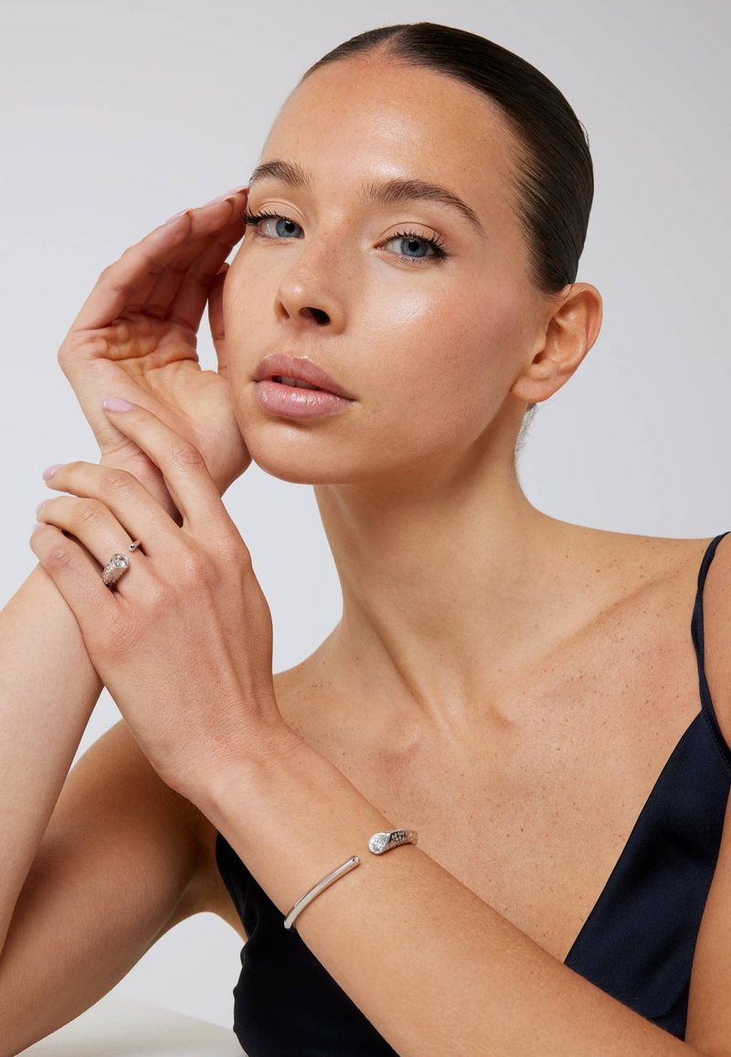 Zilveren armband met een slangdesign voorzien van sprankelende accenten, gedragen op een arm met een gladde, lichte huidskleur. Eenvoudige, elegante styling.