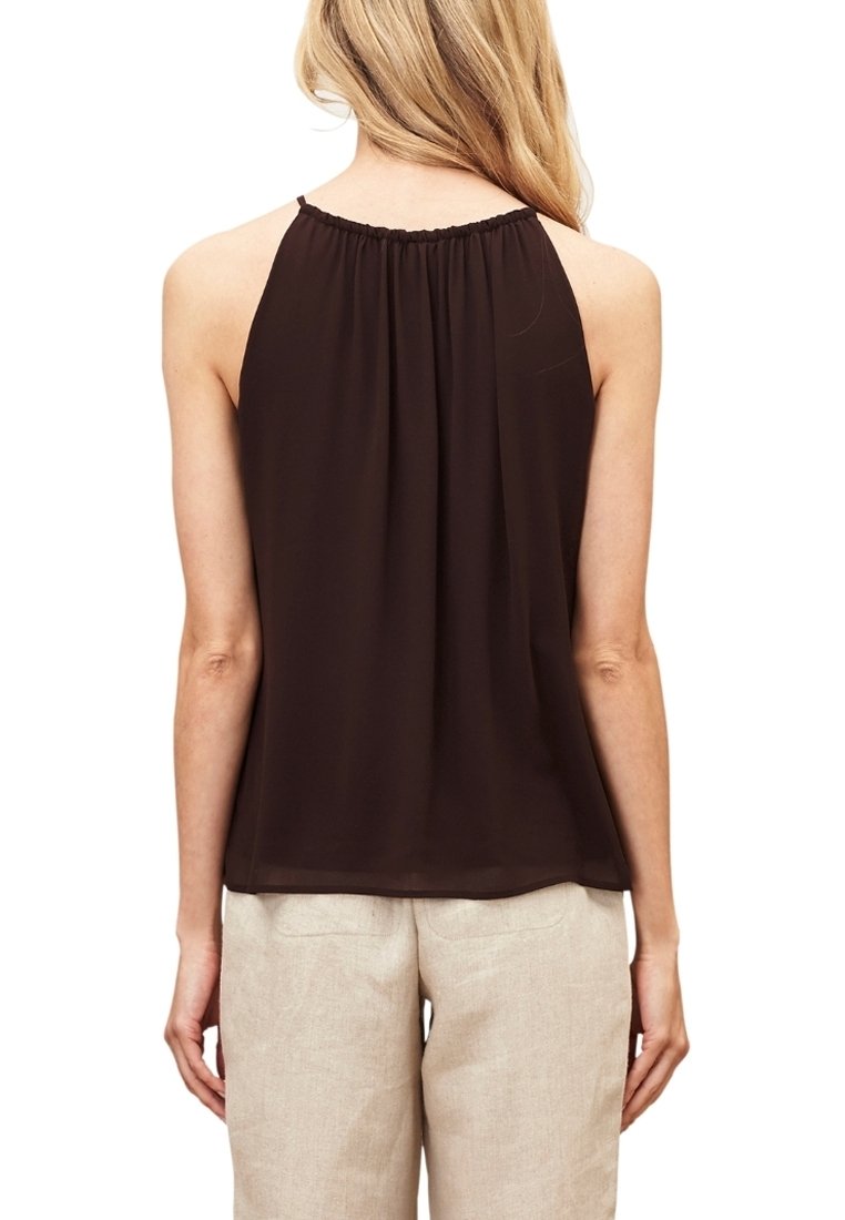 Brązowa bezrękawnikowa bluzka z marszczonym dekoltem, wykonana z lekkiego materiału, ma luźny krój i sięga tuż poniżej talii, zestawiona z beżowymi spodniami.