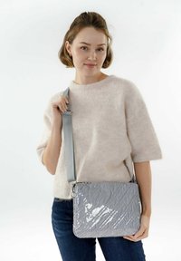 Bolso acolchado gris hecho de un material brillante, con una correa desmontable y forma rectangular. El bolso tiene una superficie texturizada y brillante.