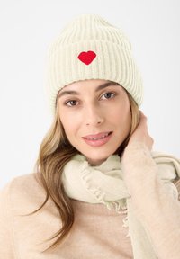 Gebreide beanie in lichtgroen met een rood hartembleem. Zachte textuur, geribbelde design, gecombineerd met een lichtgroene franjeriool.