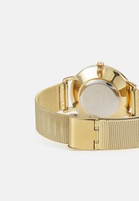 Montre en or avec un bracelet en maille, un boîtier rond et une finition polie. Comprend un fermoir et un dos lisse et réfléchissant.