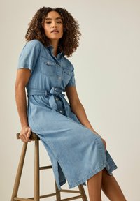 Denim pitkä paitamekko vaaleansinisessä, lyhyillä hihoilla, nappisulkimella, kahdella rintataskulla, kuminauhalla vyötäröllä ja sivuhalkioilla.