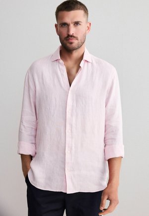 Light pink linen shirt with a relaxed fit, button-down front, and rolled-up sleeves, featuring a soft texture and casual design.