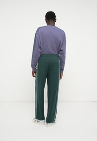 Purple sweatshirt with relaxed fit, paired with green wide-leg pants featuring side stripes and a back pocket. Sneakers with a patterned design.