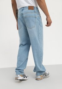 Jeans din denim de un albastru deschis, cu croială dreaptă, care au două buzunare la spate și o etichetă din piele maro la talie. Asortați cu adidași argintii.