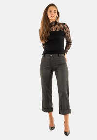 Top negro de manga larga con detalles de encaje, combinado con pantalones cortos a rayas grises, con puños enrollados y tacones negros.