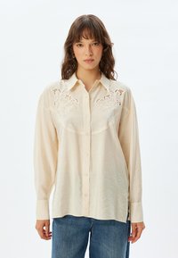 Crème blouse met lange mouwen, knoopsluiting aan de voorkant en gedetailleerde borduursels op de schouderstukken. Zachte, gestructureerde stof en een losse pasvorm. Casual ontwerp.