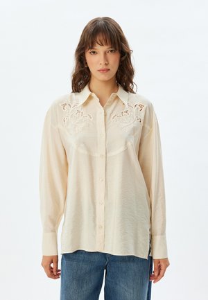 Crème blouse met lange mouwen, knoopsluiting aan de voorkant en gedetailleerde borduursels op de schouderstukken. Zachte, gestructureerde stof en een losse pasvorm. Casual ontwerp.
