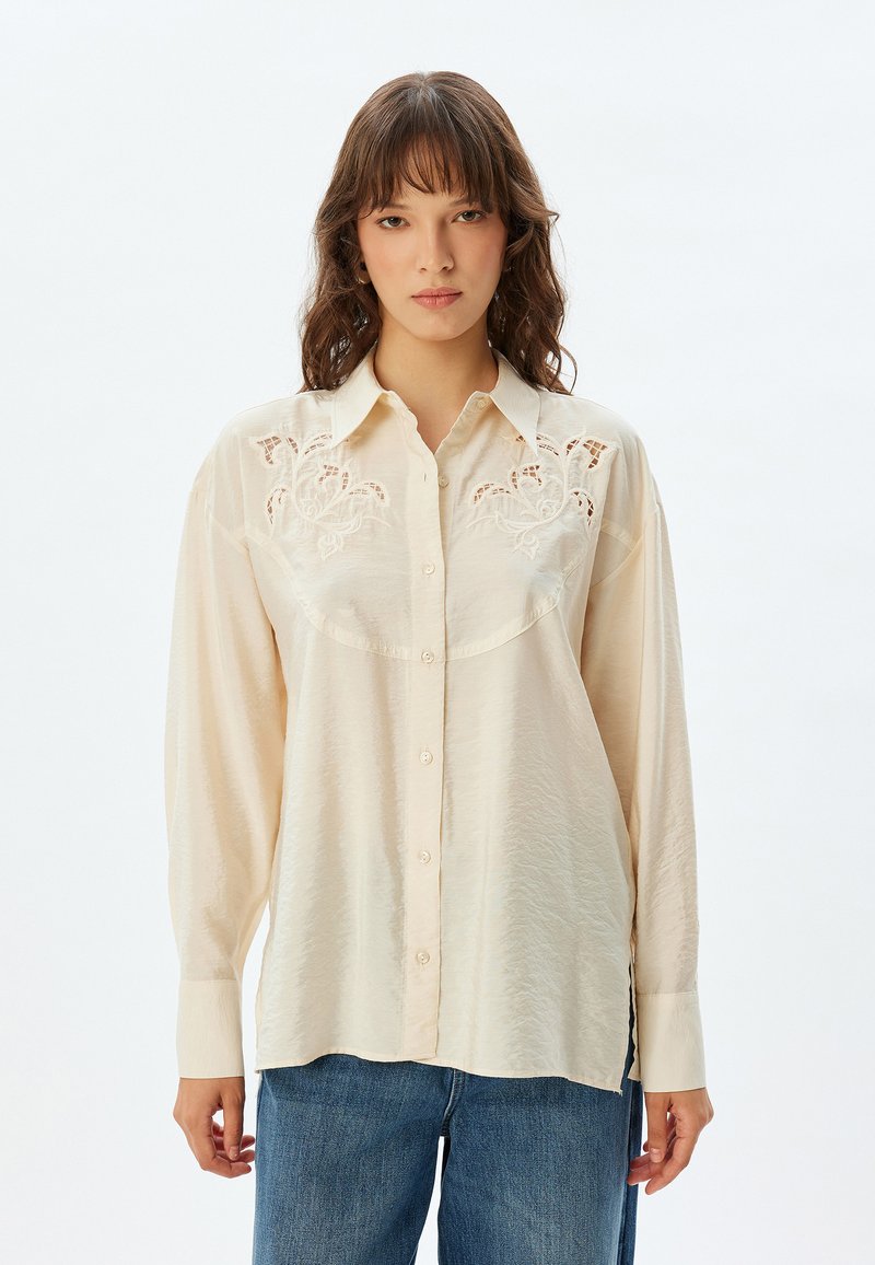 Crème blouse met lange mouwen, knoopsluiting aan de voorkant en gedetailleerde borduursels op de schouderstukken. Zachte, gestructureerde stof en een losse pasvorm. Casual ontwerp.