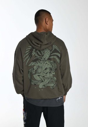 Grøn hættetrøje med en stor grafisk design af et skelet med slanger og en ørn på ryggen. Blødt stof, afslappet pasform.