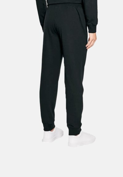 Pantalons de jogging noirs avec une taille élastique, ourlets resserrés et une texture lisse, accompagnés de chaussures de sport blanches.