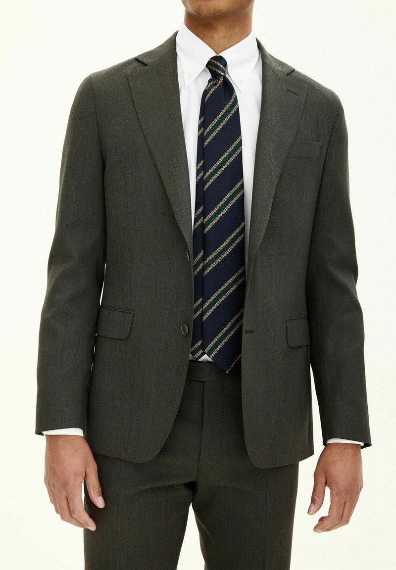 Mörkgrön skräddarsydd kostym med notch-lapel, två framfickor och en vit skjorta. Mönstrad blå och gul slips ger extra detaljer.