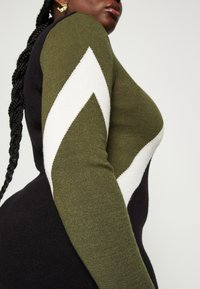 Abito lavorato a maglia caratterizzato da colori verde scuro e nero con un motivo a zig-zag bianco sulla manica, tessuto testurizzato e una silhouette aderente.