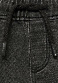 Svarta denimbyxor har en svart flätad dragsnodd i midjan, med en slät yta och diskreta sömnadsdetaljer nära fickan.