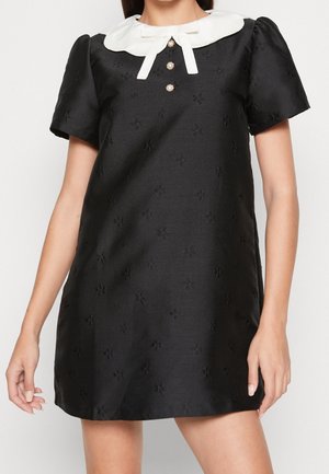 Robe noire à manches courtes avec une texture florale subtile, col Peter Pan blanc, trois boutons en perle et un petit nœud décoratif blanc.