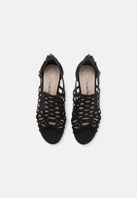 Paire de sandales à talons noires avec brides, orteils ouverts et sangles à la cheville, vues de dessus sur un fond clair uni.