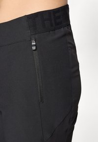 Black athletic pants with a stretchy waistband and a side zipper pocket. The fabric has a smooth texture and a fitted design.