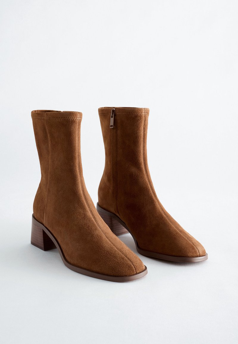 Paire de bottines en daim marron à talons carrés avec fermetures éclair latérales sur fond blanc