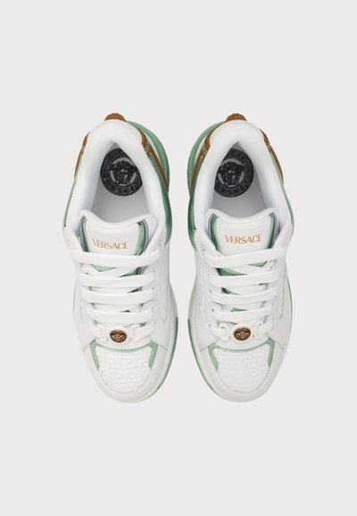 Ζευγάρι λευκά και πράσινα sneakers Versace με κορδόνια, χρυσό έμβλημα Μέδουσας στη μύτη και το λογότυπο Versace στη γλώσσα, από πάνω.