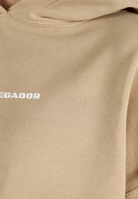 Hanorac de culoare maronie, realizat dintr-un material moale din amestec de bumbac, având o buzunar frontal și logo-ul „LEGADOR” în text alb pe zona pieptului.