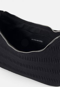 Sort tekstureret clutch taske med en bølget design, sølv lynlås lukning og en glat inderside med en mærkelabel.