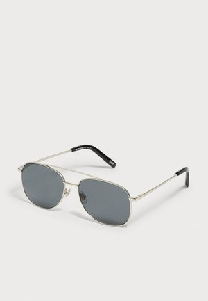 Sonnenbrille mit silbernem Metallrahmen, rechteckigen dunkelgrauen Gläsern und schwarzen Bügelenden, gezeigt vor einem hellen neutralen Hintergrund.