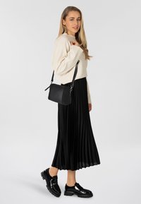 Zwarte geplooide rok, crèmekleurige trui en zwarte leren schoudertas; glanzende zwarte plateau schoenen maken de look compleet.