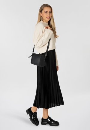 Falda negra plisada, suéter crema y bolso de hombro de cuero negro; unos zapatos de plataforma negros brillantes completan el atuendo.