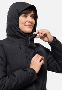 Schwarze wasserdichte Jacke mit hohem Kragen und verstellbarem Kapuze, ausgestattet mit einem Frontreißverschluss, Zugkordel und engen Bündchen. Sanfte Textur und minimales Design.
