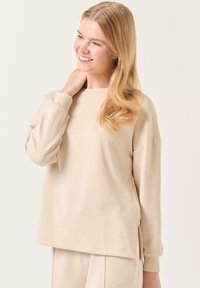Felpa beige con maniche lunghe, polsini a coste e fessure laterali. Tessuto morbido e liscio con una vestibilità comoda e scollatura a girocollo.