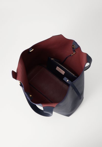 Sac fourre-tout en cuir bleu marine avec un intérieur bordeaux, doté d'une poche zippée et d'un compartiment plat, avec des accents en métal doré.