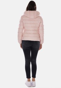 Giacca puffer rosa chiaro con cappuccio, design trapuntato e polsini a costine, abbinata a jeans skinny neri e sneakers bianche.
