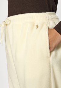Krämfärgade fleecebyxor med dragsko i midjan, sidofickor och en broderad logotyp på vänster lår. Mjuk textur, avslappnad passform.