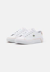 Pair of white low-top sneakers with light pink accents, lace-up design, and green crocodile logo on the side against a white background.