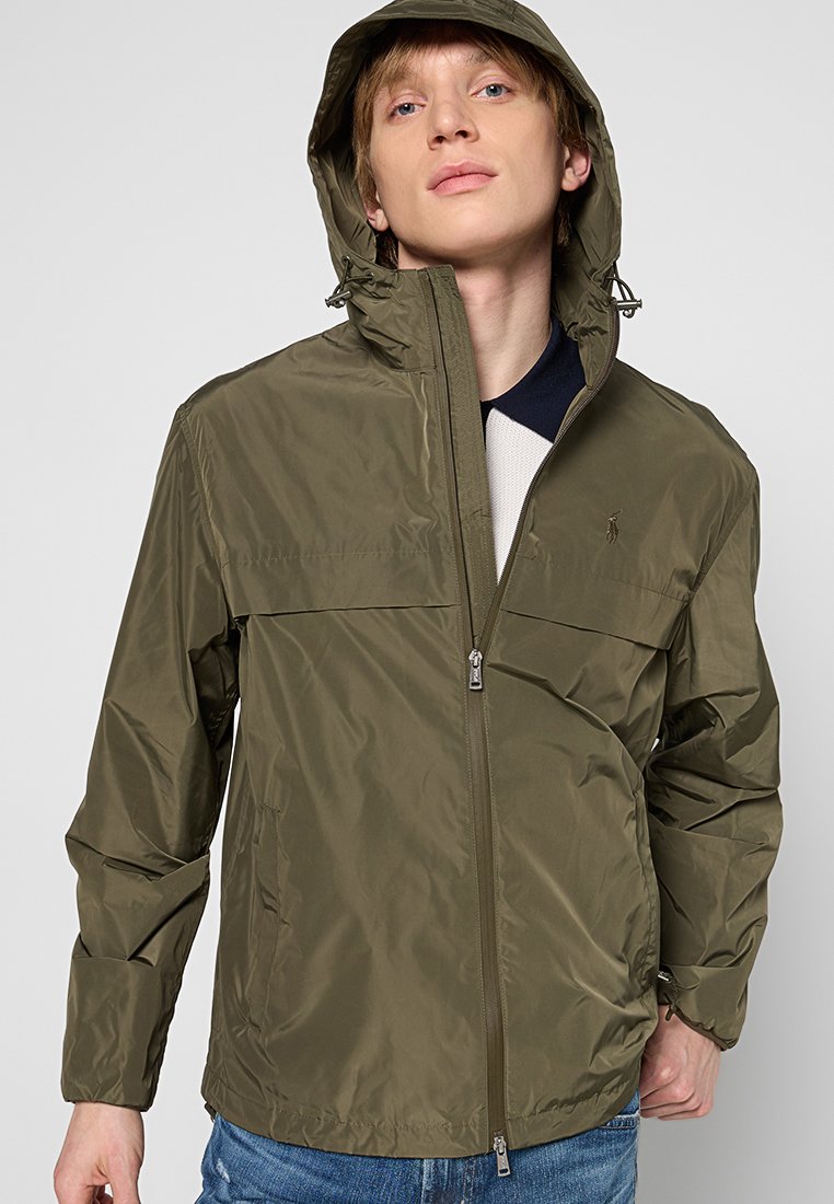 Olivgrüne, wasserfeste Jacke mit Kapuze, Reißverschluss und zwei Seitentaschen. Glatte Textur und leichtes Design, geeignet für den Einsatz im Freien.
