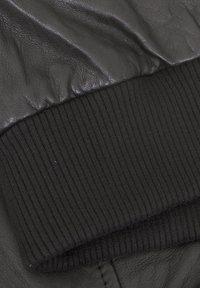 Schwarzes Lederstoff mit einem gerippten, schwarzen Strickbündchen, das eine glatte Oberfläche, einen leichten Glanz und eine geraffte Textur entlang der Kante aufweist.