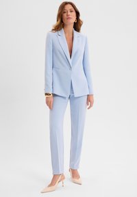 Jasnoniebieski garnitur o dopasowanym kroju z marynarką i prostymi spodniami. Gładki materiał, minimalistyczny design, z pojedynczym zapięciem na guzik.