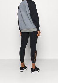 Grå och svart sweatshirt med ribbad nederkant, kombinerad med figurnära svarta leggings med utskärningar längs sidan, bärs med svarta sneakers.