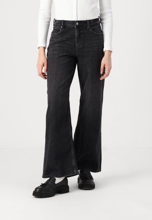 High-waisted black denim flared jeans with front pockets, faint texture, and a button closure. Paired with black loafers and a white top.