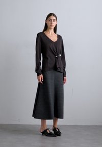 Black long-sleeve top with a V-neck and twist detail, paired with a grey, knee-length skirt. Black shoes with decorative ties.