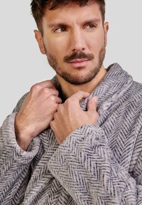 Ropa de gris con patrón de espiga, hecha de tela suave, con un cuello de chal y mangas dobladas, llevada cómodamente alrededor del cuello y los hombros.