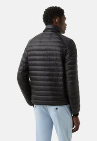 Sort dunjakke med quiltet design, høj krave og elastiske manchetter. Glat tekstur, let vægt og tætsiddende med en moderne silhuet.