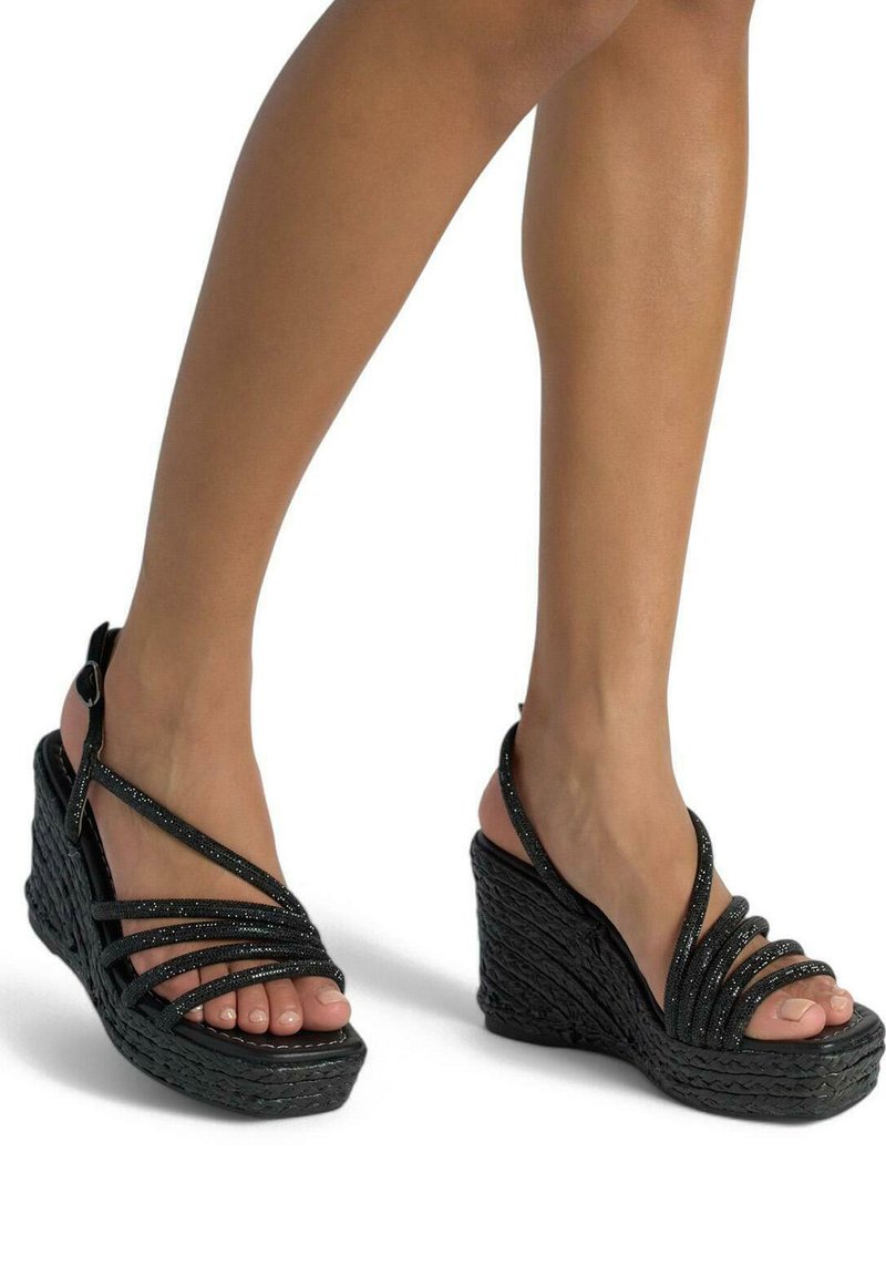 Las sandalias wedge negras presentan una plataforma texturizada, múltiples tiras finas con un acabado brillante y un diseño de punta abierta. Incluye una correa para el tobillo ajustable.