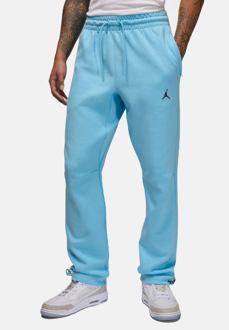 Jasnoniebieskie spodnie dresowe z elastycznym pasem i sznurkiem do regulacji. Na lewej łydce znajduje się czarne logo, a szwy mają kontrastujące kolory.