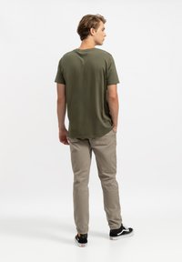 Olijfgroene t-shirt met korte mouwen, reguliere pasvorm en een gladde textuur. Gekleed met lichte beige broek en zwarte sneakers.