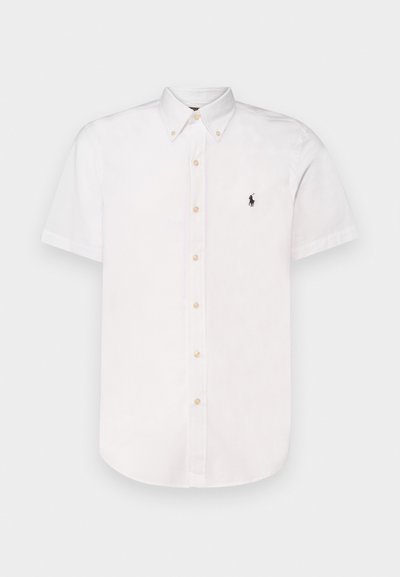 Chemise blanche à manches courtes, en coton, avec un col pointu, des boutons beiges et un petit logo noir brodé sur la poitrine.