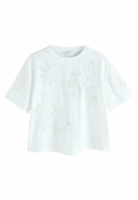 T-shirt en coton blanc à manches courtes, avec broderie florale dans une finition légèrement texturée. Encolure ras du cou classique et coupe décontractée.