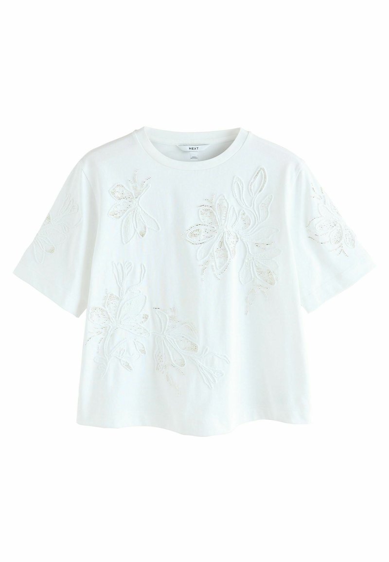 T-shirt en coton blanc à manches courtes, avec broderie florale dans une finition légèrement texturée. Encolure ras du cou classique et coupe décontractée.