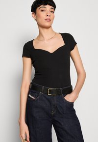 Bodies noir côtelé avec décolleté carré, associé à un jean bleu foncé et une ceinture noire avec une boucle dorée.