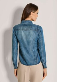 Denim shirt in een middelblauwe tint, met een puntige kraag, lange mouwen en een gebogen zoom, met subtiele stiksels langs de naden.